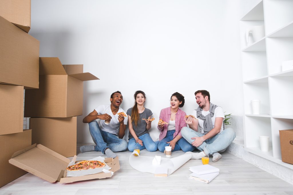 Friends and family sitting in a new home after helping each other move with boxes and pizza party