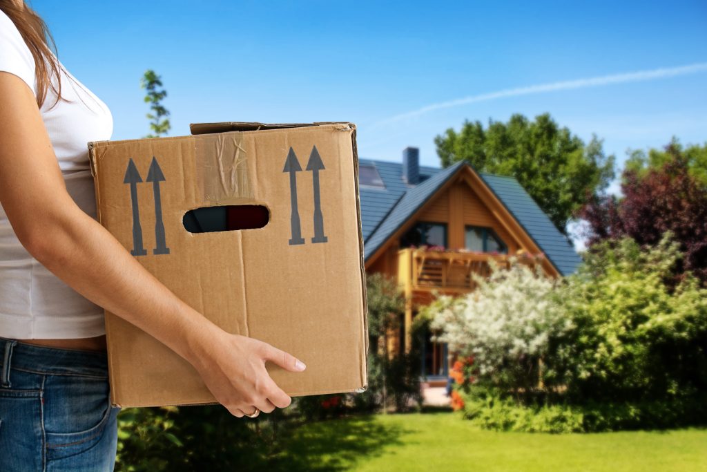 Closeup of woman's hands holding a moving box with rural house in the background